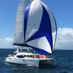 A white and blue sailboat gliding on the ocean under clear skies.