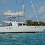 White sailing catamaran on calm blue water near green island.