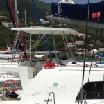 A white catamaran docked at a marina with fishing rods and hills in the background.