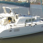 White catamaran sailboat docked in calm water near a marina.
