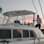 Person standing on a boat at sunset with a pink sky.