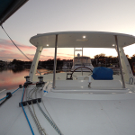 View from a sailboat deck at sunset with calm waters and ropes.