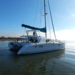A white catamaran anchored on calm water under a clear sky.