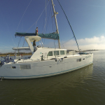 A white sailboat docked on calm water under a clear blue sky.