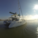 A white catamaran yacht anchored on calm water under a bright sky.
