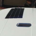 Small solar panel installed on a white vehicle roof.
