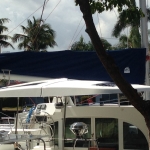 Yacht docked near palm trees under cloudy sky.