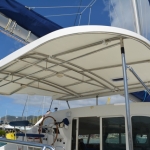 White canopy over a boat's upper deck with a person steering below.