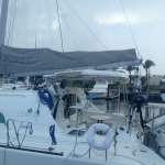 Sailboat docked with fishing rods and covered sails at marina.