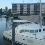 A white catamaran docked by a waterfront building on a sunny day.