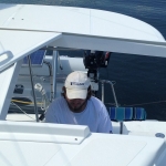 Man steering a boat on calm water under sunny weather.