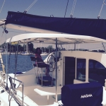 A man steering a sailboat on a sunny day with scenic water views.