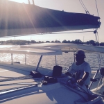 Person relaxing on a sailboat during sunset on calm waters.