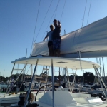 Two people standing on a sailboat under a clear blue sky.
