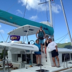 Three people posing on a sailboat under a clear blue sky.
