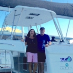 Two friends smiling on a boat with a marina background.