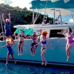 Group of people jumping into the water from a boat on a sunny day.