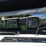 View of a boat's cabin with windows and a sunshade on a sunny day.