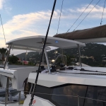 A yacht docked near a coastal town at sunset with hills in the background.