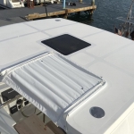 Boat deck with a hatch and a folded sunshade near the water.