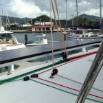 View from a sailboat docked at a marina with other boats and mountains in the background.