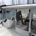 Two men sitting under a canopy on a boat near the dock.