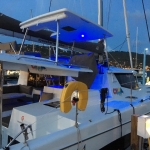 A sleek white yacht docked at night with blue lights and a sunny life ring.