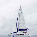 Sailboat with white sails on calm water under a cloudy sky.