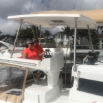 Person steering a boat near a marina with cloudy skies.