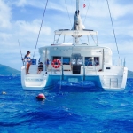 A white catamaran anchored in clear blue ocean waters with people on board.