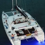 White catamaran yacht sailing on calm water with people relaxing.