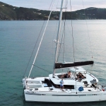 A white catamaran sailing on calm blue waters near hilly shores.