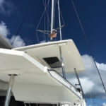 Sailor adjusting ropes atop a white sailboat under a blue sky.