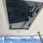 Boat ceiling hatch with a reflective glass panel and blue sky in the background.