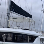 Close-up of a white catamaran sailboat with a black sail cover docked in a marina.