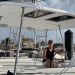 Woman steering a boat under a partly cloudy sky at the marina.