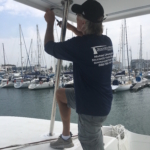Man adjusting boat rigging at a marina filled with sailboats.
