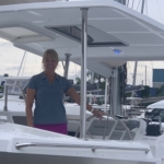 A woman standing on a white boat docked at a marina.
