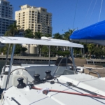 Sailboat deck with marina and buildings in the background under clear blue sky.