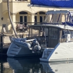 A white catamaran docked at a marina with a blue canopy.