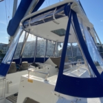Sailboat cockpit with protective blue canvas and clear windows under a sunny sky.