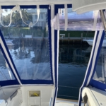 View from inside a boat cockpit looking out through clear plastic and blue canvas covers.