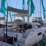 A white catamaran docked at a marina under teal sails.