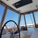 View from inside a boat cockpit showing the steering wheel and marina outside.