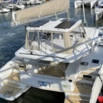 A white catamaran docked at a marina with other boats.